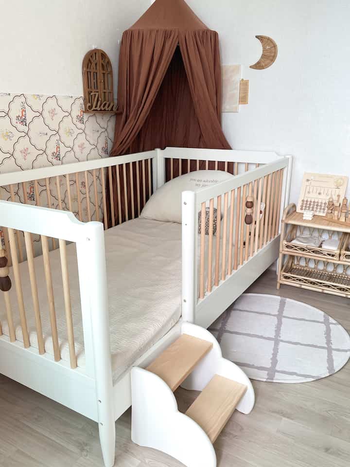 木目調と白を基調とした赤ちゃん部屋、クリーム色のベッドとステップスツール、ラウンドラグが配置された温かみのあるインテリア