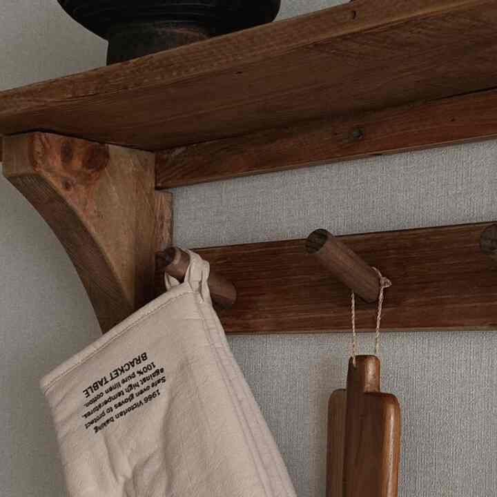Vintage style kitchen space featuring brown wood-tone wall-mounted shelf and hanging oven mitts with a natural atmosphere