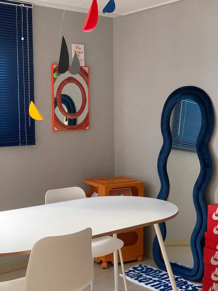 ネイビーとホワイトの色調のダイニング、白いダイニングテーブルと椅子、独特な波型のネイビーの鏡、多彩なモビールが配置された雰囲気ある空間