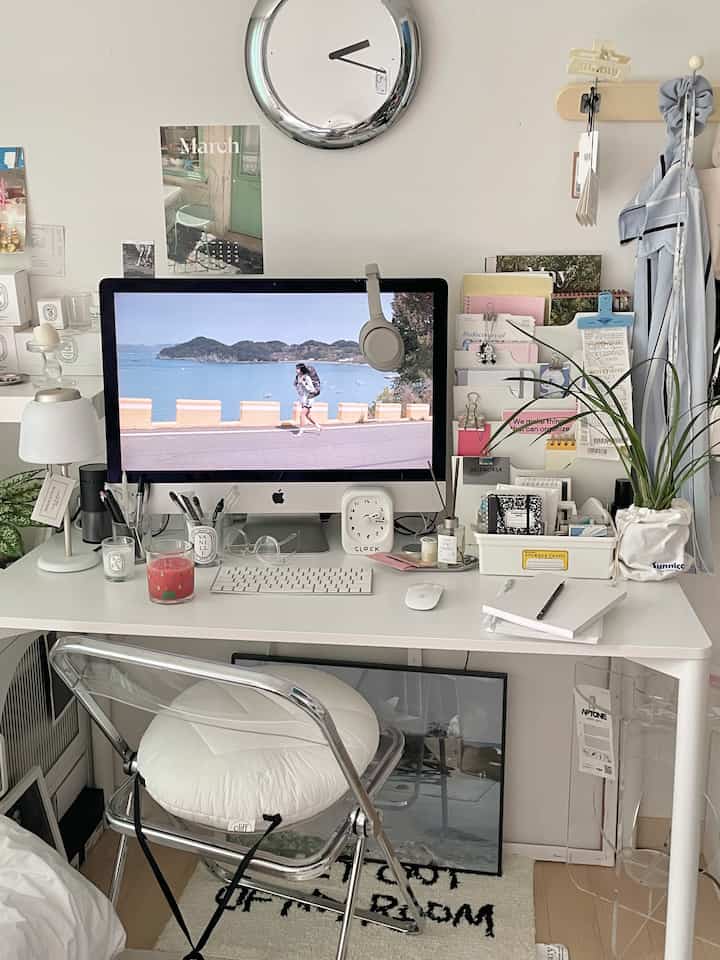 White-toned home office space featuring a computer and transparent folding chair arranged on a tidy desk
