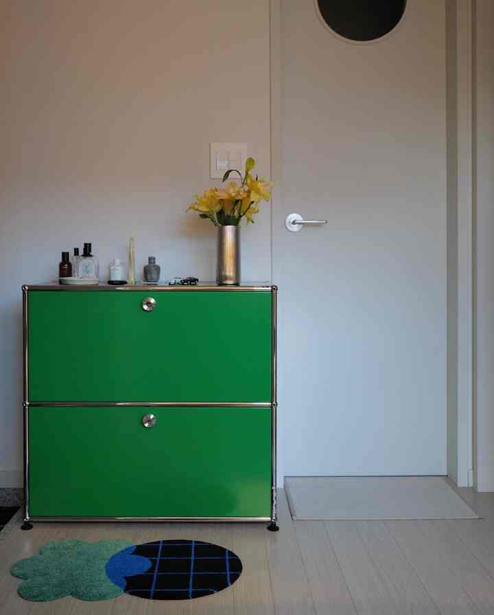 緑のサイドボードと蛍光色の花瓶、床にパターンのあるラグマットが置かれた整った玄関スペース
