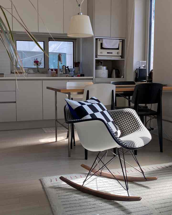 Modern kitchen and dining room in white and black tones featuring a rocking chair with checkered cushions creating a cozy atmosphere