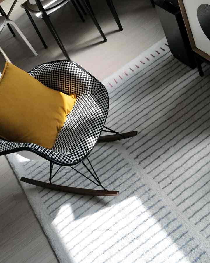 Natural-toned living room with a square rug featuring light gray and blue lines, and a checkered rocking chair topped with a mustard cushion