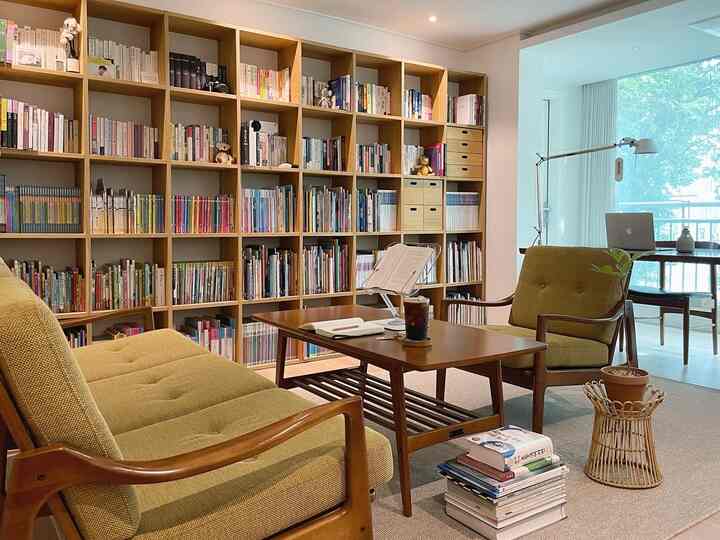 Beige and wood tone living room study featuring large bookshelf, cozy sofa, and a home cafe vibe with coffee on the table