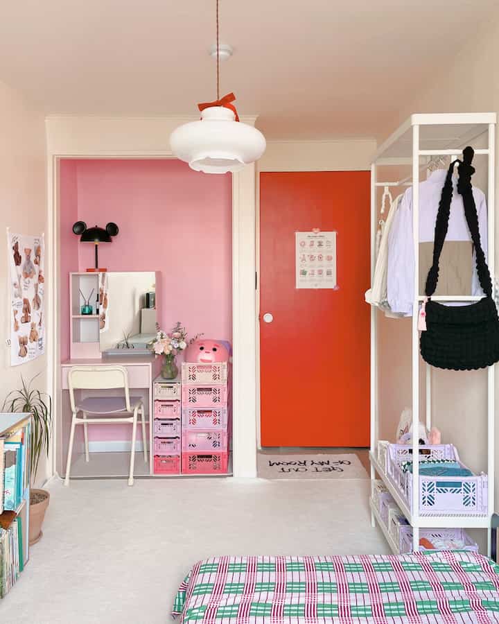 白を基調とし、ピンクのアクセント壁と赤いドア、デスクや収納ボックスが配置された雰囲気のある子供部屋