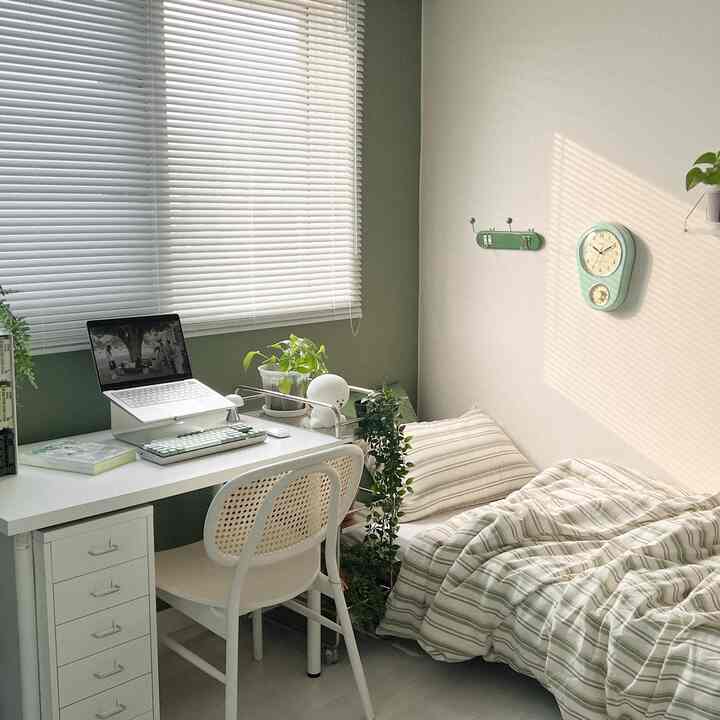 White and green toned small single household room featuring desk, bed, and plants with a natural atmosphere for remote work