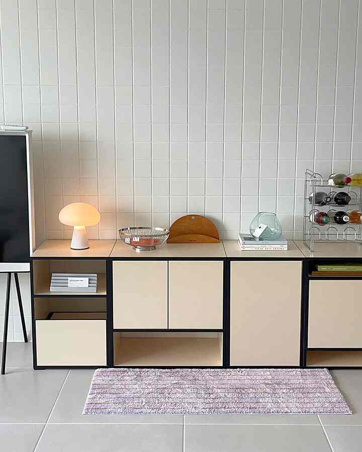 ベージュトーンのリビング空間、モジュラー収納キャビネットとワインラック、ポータブルテーブルランプが配置されたシンプルでナチュラルな雰囲気のインテリア