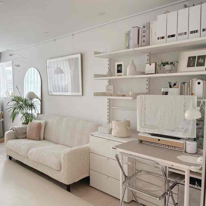 Bright white-toned living room featuring a cream sofa, modular dresser, and desk in a neat natural interior