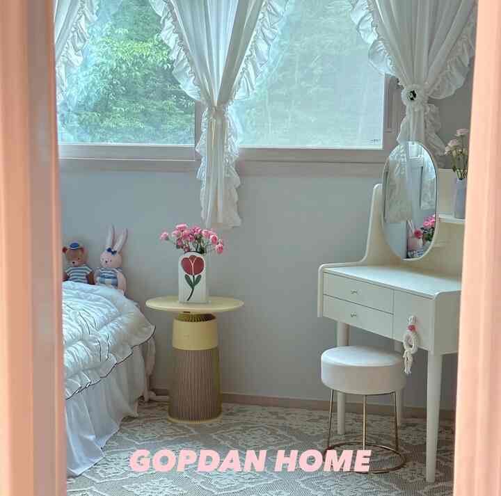 明るいホワイトトーンの子供部屋、白いベッドと化粧台、ピンクの花飾りが配置された落ち着いた空間