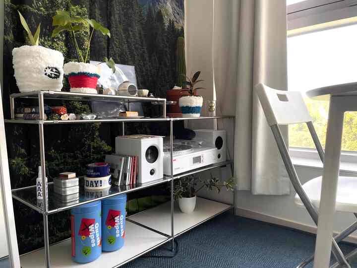 Blue and white toned studio apartment featuring a metal shelving unit and white folding chair in a clean, cozy setting