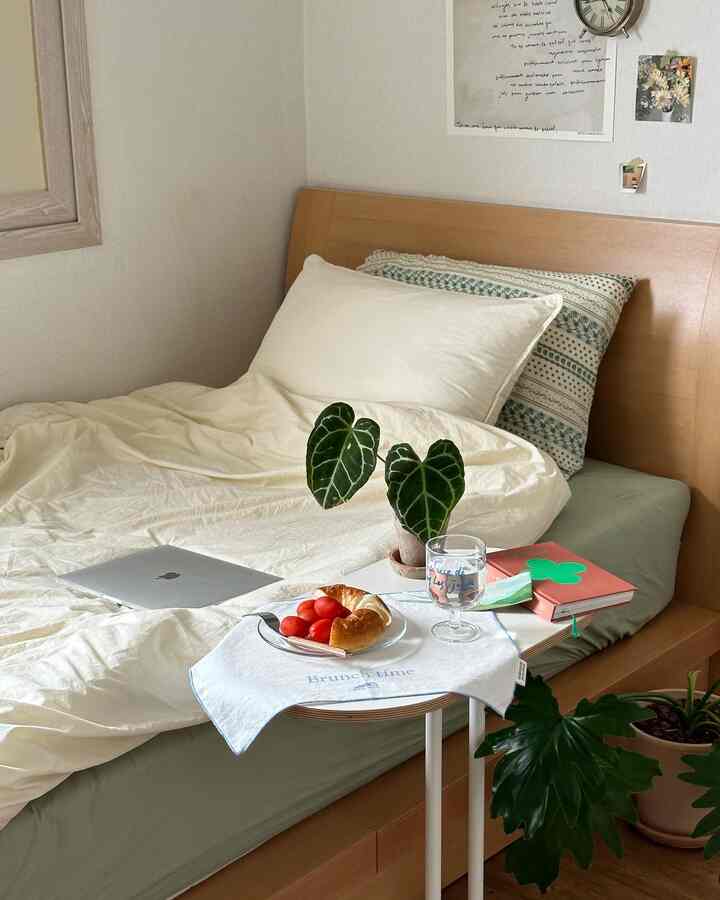 Beige-walled bedroom with wooden bed, white duvet cover and plants arranged in cozy natural setting
