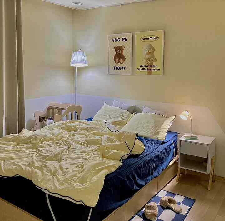 黄色い壁とネイビーの寝具が印象的な寝室、小さな木製の椅子に座る猫がいる雰囲気のあるインテリア