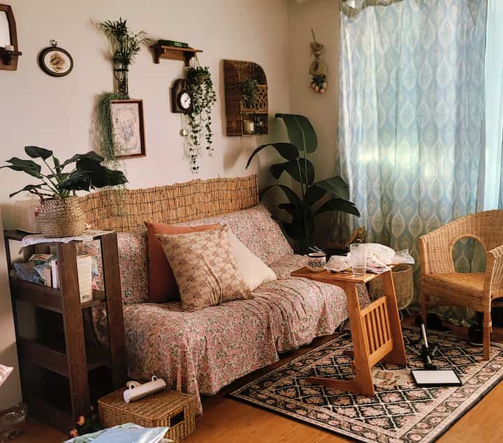 温かみのある木目調の床とヴィンテージの花柄ソファが配置された居心地の良いリビング、植物とカーテンが温かな雰囲気を演出しているインテリア