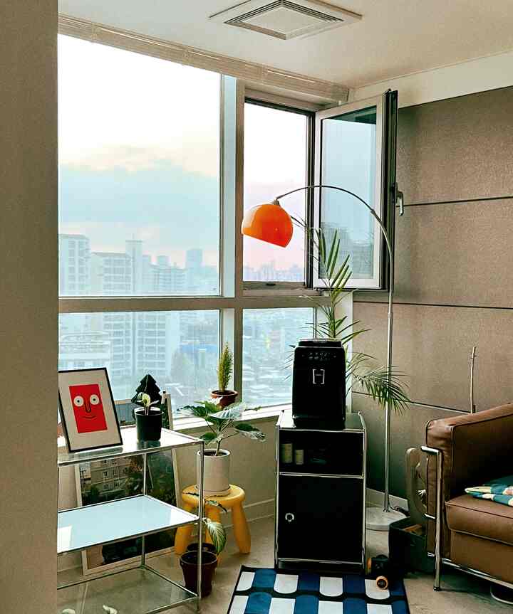 White and blue toned living room corner featuring orange floor lamp, coffee machine, and plants in a natural modern style