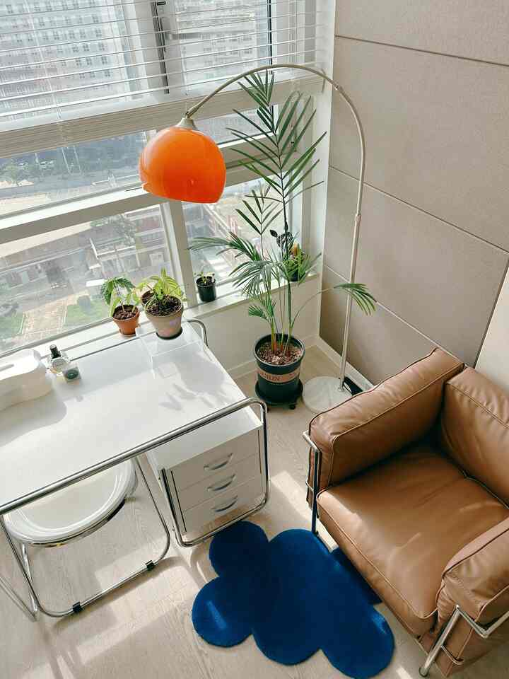 White and wood-toned living room with orange lamp and leather sofa, plants adding natural warmth to cozy space