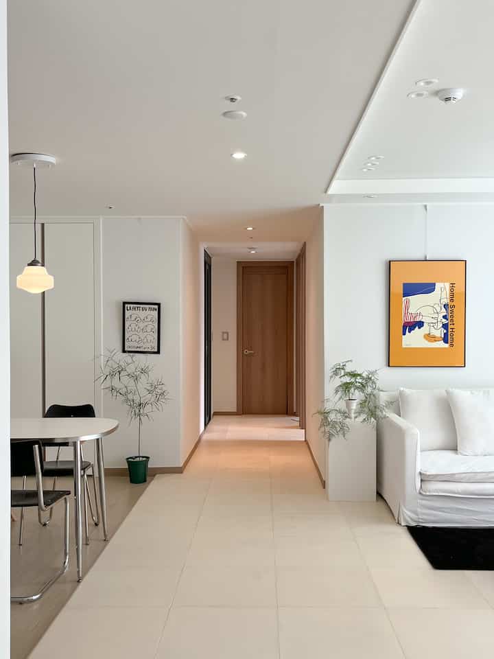 白とベージュを基調としたリビング、ミッドセンチュリーモダンのポスターとファブリックソファ、ダイニングテーブルと植物が配置されたシンプルでスタイリッシュなインテリア