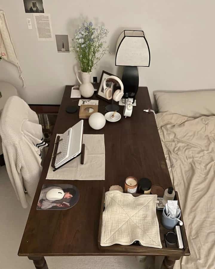 Beige-toned studio apartment bedroom combined with home office, featuring a walnut wood desk and lamp for a cozy atmosphere