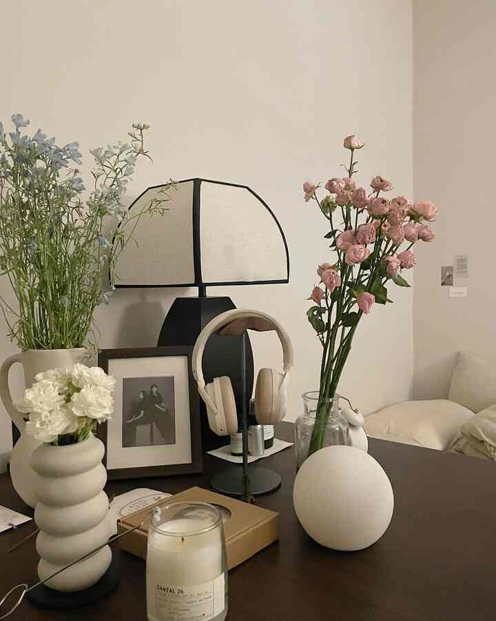 ベージュとホワイトのトーンのテーブル上に花瓶や照明、ヘッドフォンが配置されたシンプルでナチュラルなインテリア空間