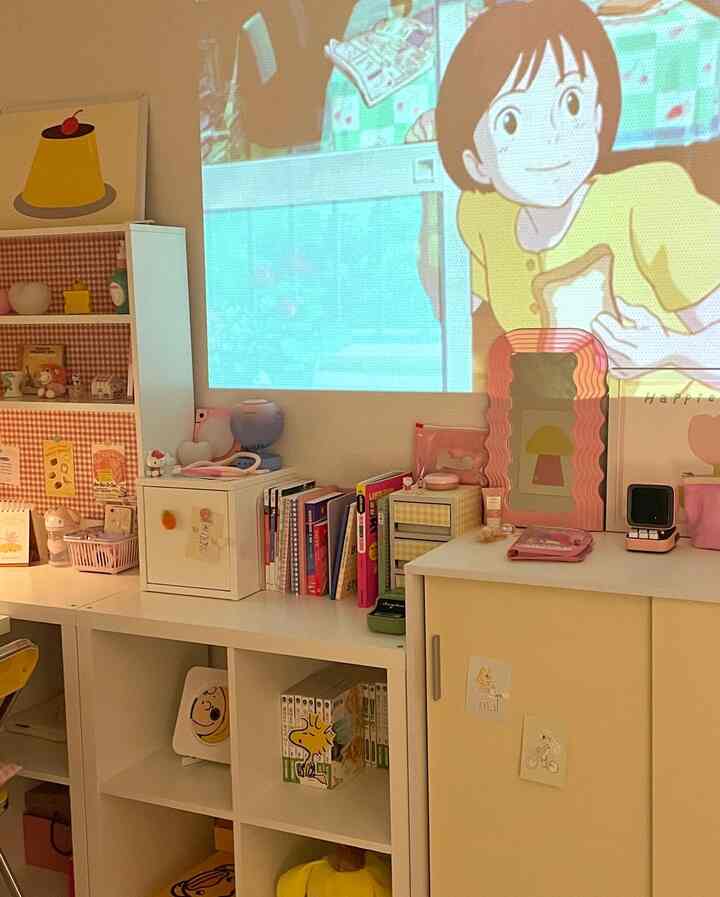 白と黄色の色調の子供部屋、整然とした本棚とキャビネット、壁にアニメが投影された雰囲気のあるインテリア