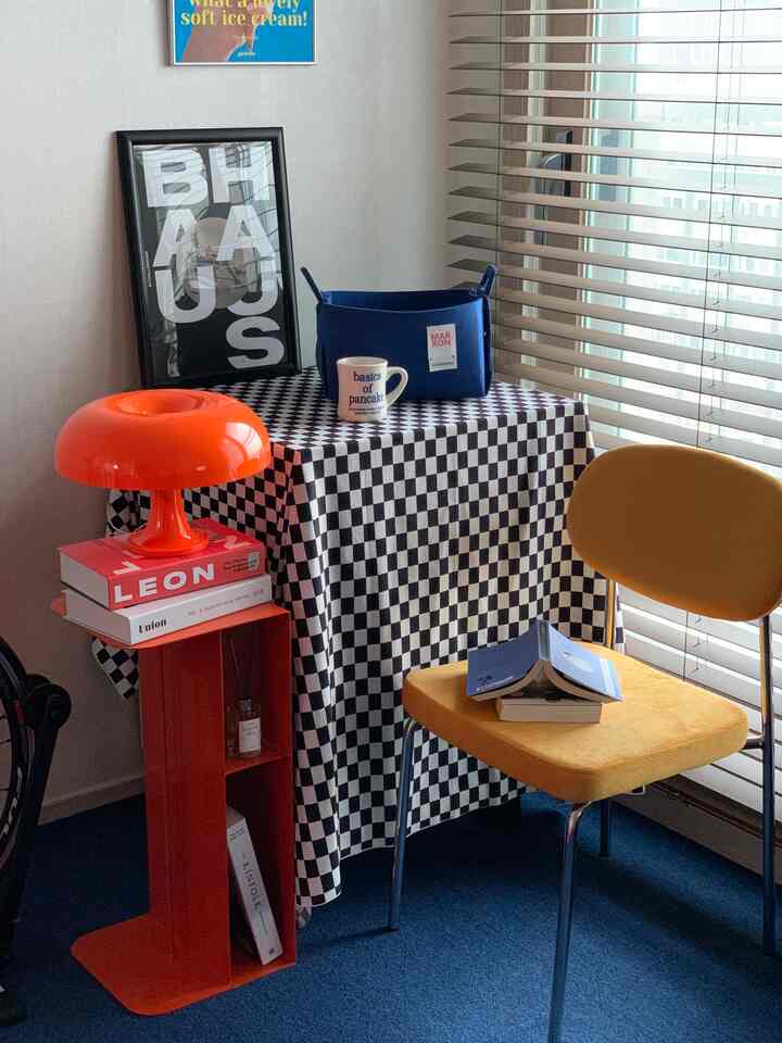 オレンジのテーブルランプと黄色い椅子がある青いカーペットの空間、チェック柄テーブルクロスが置かれたミッドセンチュリーモダンのキッチン兼ホームカフェ