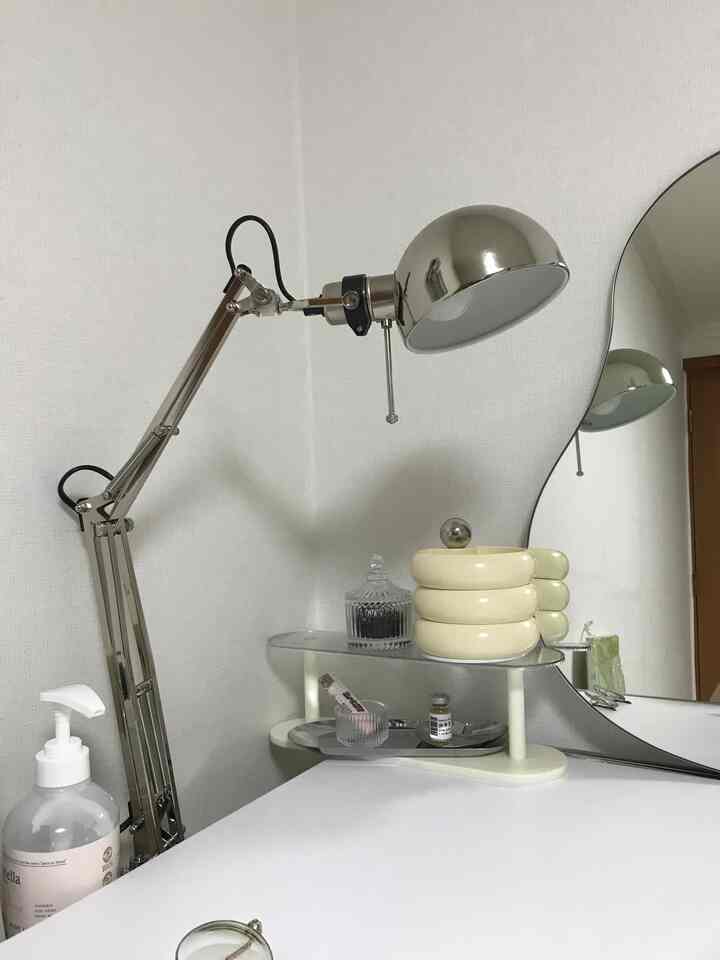 Modern desk space with dominant white and silver tones, featuring an adjustable silver lamp and a round mirror in a clean aesthetic