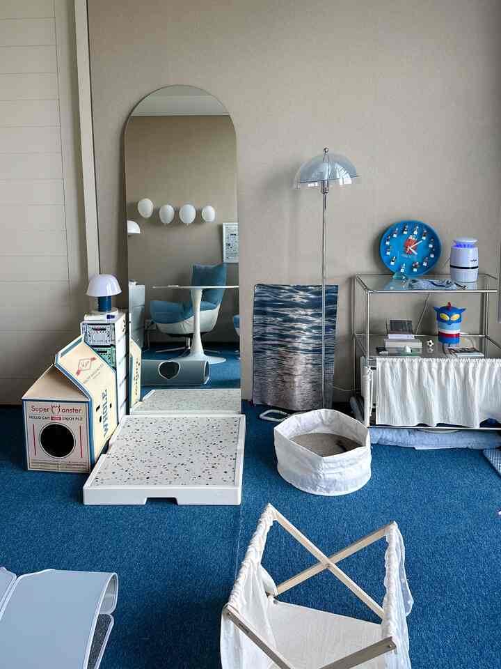 Living room with blue carpet and beige walls featuring cat hidden house and scratching post in a cozy pet-friendly interior