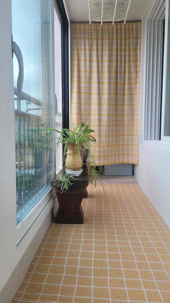 Cozy veranda featuring bright yellow checkered mat and curtain with wooden bench holding green plants