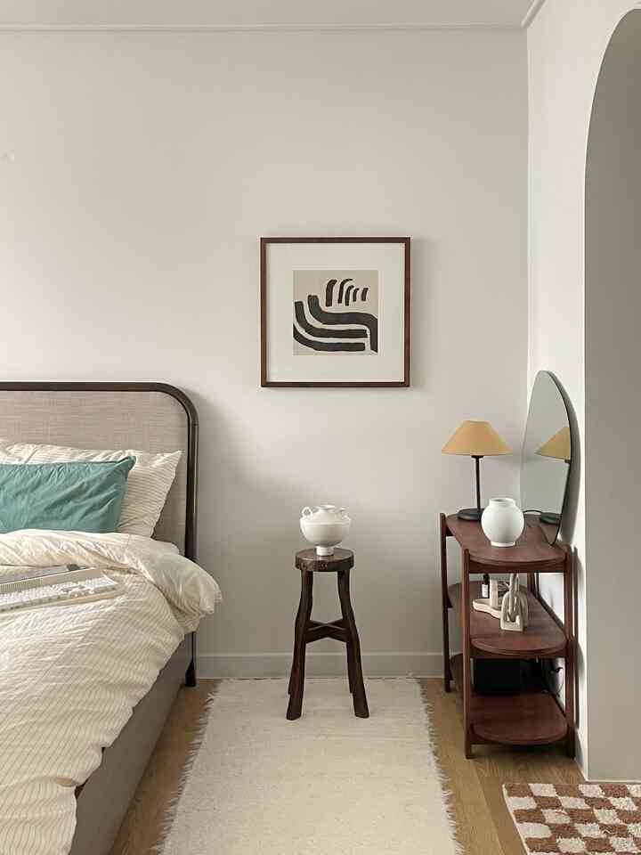 Natural bedroom with white walls and wood-tone furniture, featuring a bed, nightstand, and framed art creating a warm atmosphere