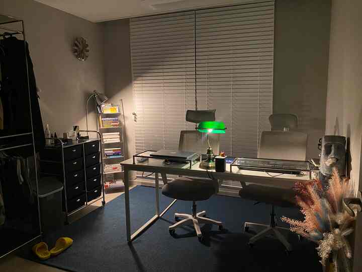 落ち着いたグレーとネイビートーンの書斎兼ウォークインクローゼット空間、中央に丸いデスクとグリーンのバンカーズランプが配置された印象的なインテリア