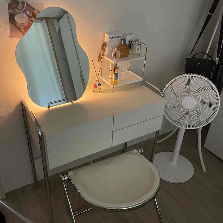 Modern vanity space featuring white and wood tones, with a uniquely shaped mirror and cosmetics on a shelf placed atop the vanity