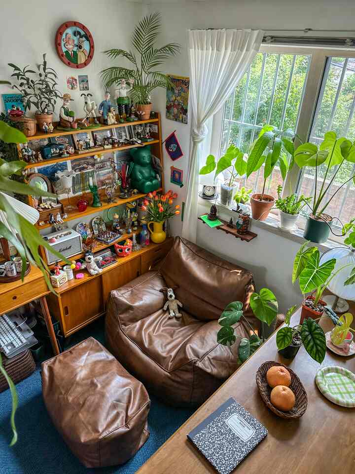 ブラウンレザーのビーズクッションソファと木製の本棚、多様な植物が配置された明るく居心地の良いリビング