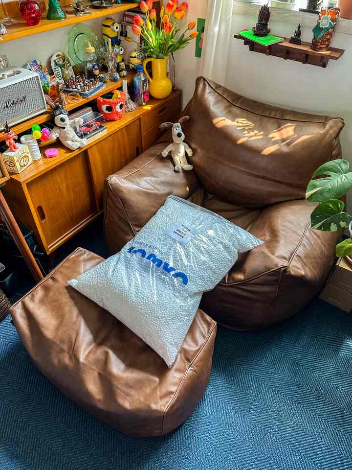 ブラウンレザーのビーズクッションとオットマンが配置された多目的なワンルーム、黄色い花瓶のチューリップと植物が置かれた温かみのあるナチュラルなインテリア