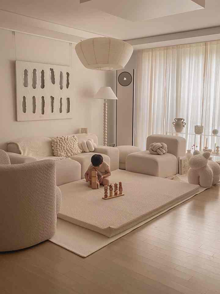 Beige-toned living room featuring a child playing on a floor mattress with natural, cozy ambiance