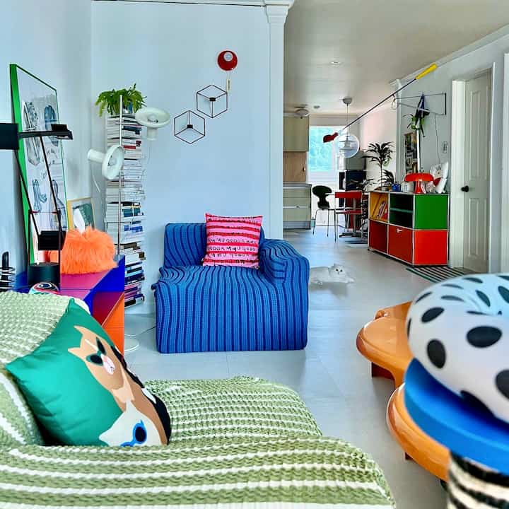 Colorful living room featuring blue and green sofas, red dining table and wall sconces creating a bright, lively atmosphere
