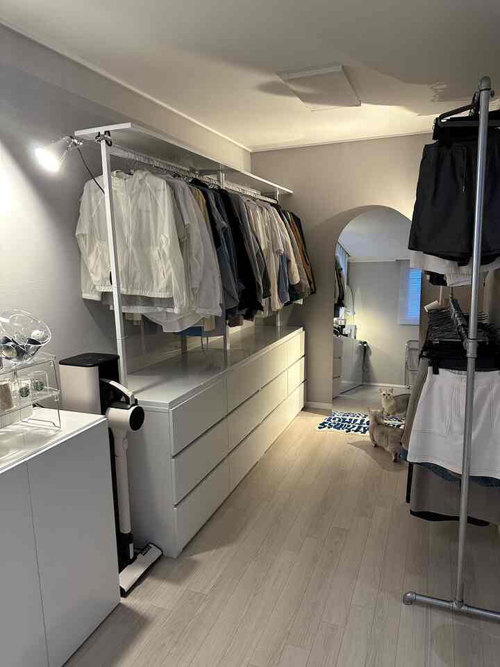 White and natural tone walk-in closet featuring organized clothing and two cats on a rug
