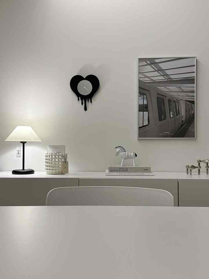 ホワイトトーンの書斎空間、テーブルランプとアルミ額縁、シンプルな白黒の時計とデコレーションが配置された清潔感のあるインテリア