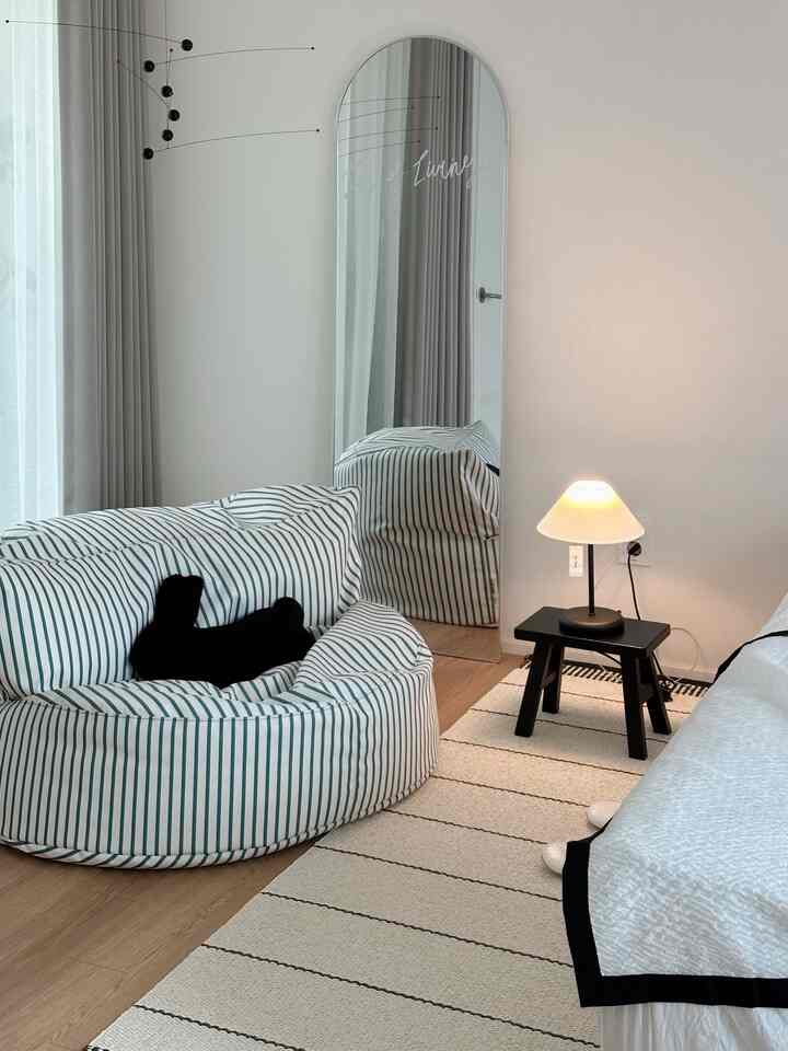 ライトブラウンの床と白い寝室、ストライプのビーンバッグとテーブルランプが配置されたナチュラルモダンなインテリア