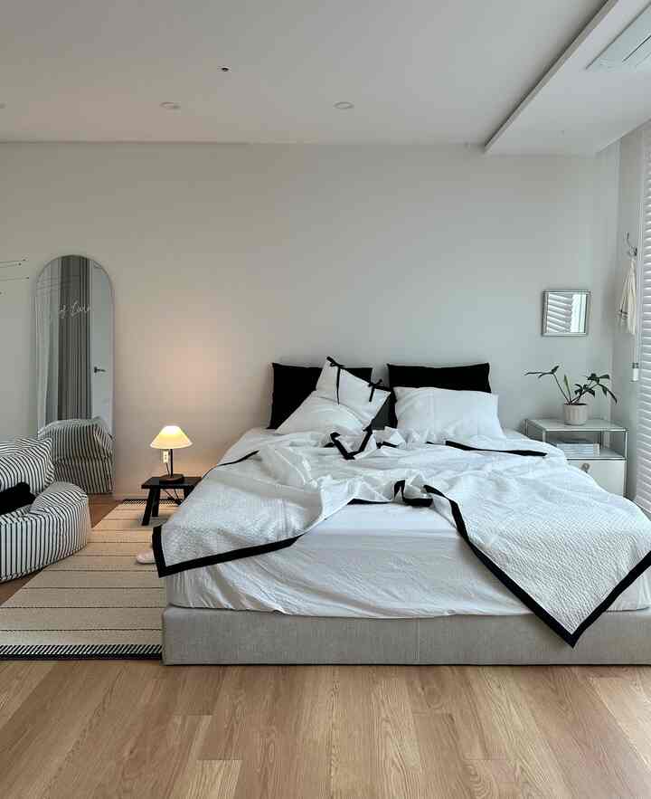 ホワイトとベージュのトーンの寝室、中央に大きなベッドとナイトテーブル、テーブルランプが配置された雰囲気のあるナチュラルモダンなインテリア