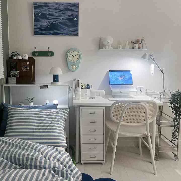 White and blue toned studio home office space featuring a striped duvet and clean desk with modern natural ambiance