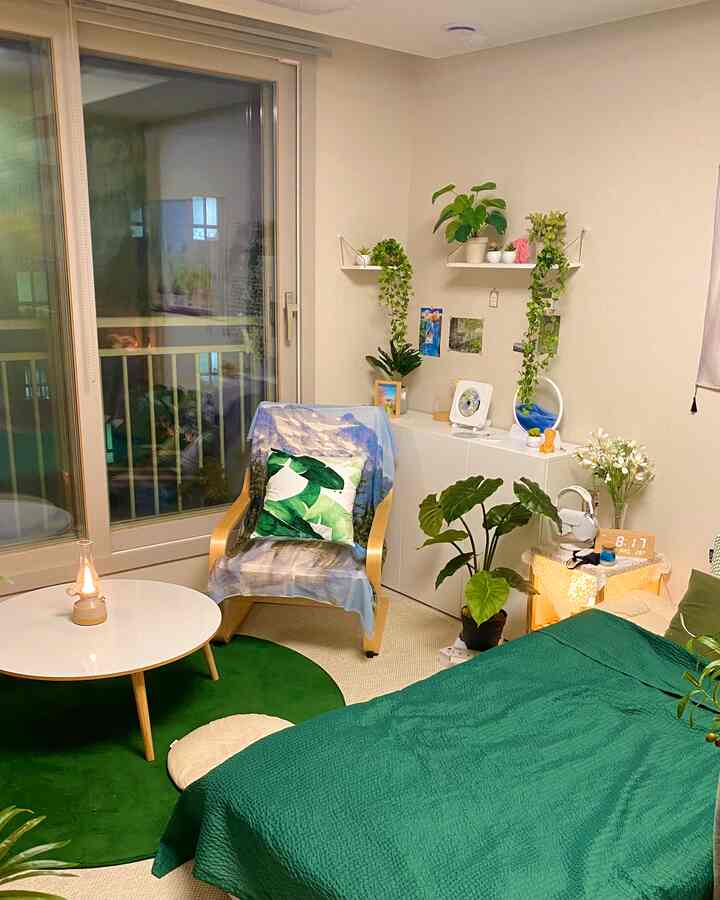 Natural-toned bedroom with green and beige hues, featuring a wooden chair, round coffee table, and multiple plants