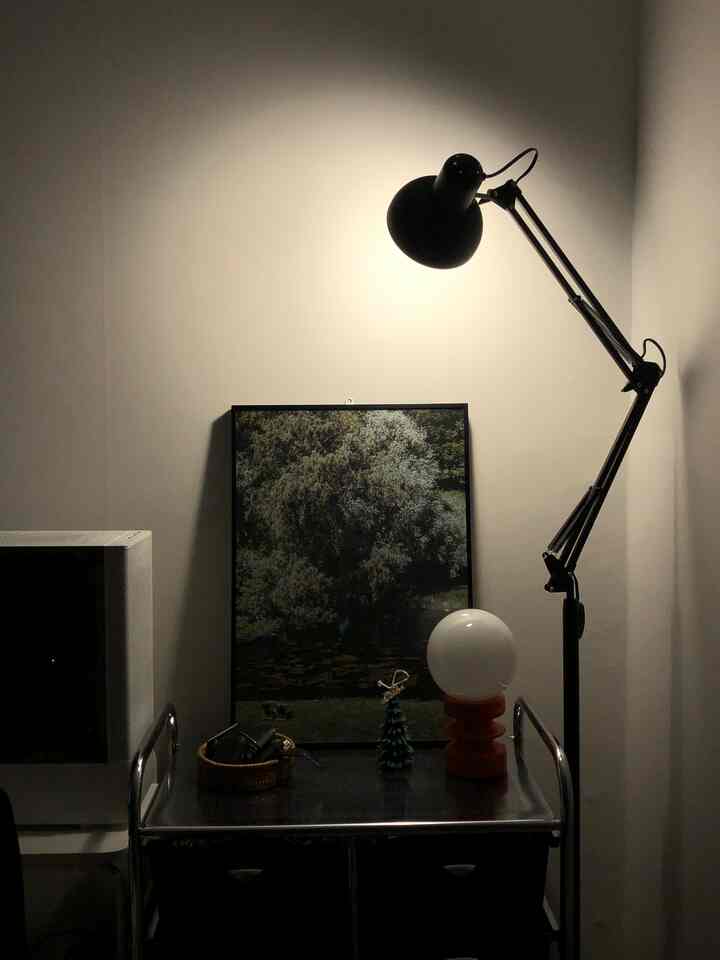 暖かな照明が灯るモダンなリビングの一角、黒のフロアランプと額縁が配置されたナチュラルな色調の空間