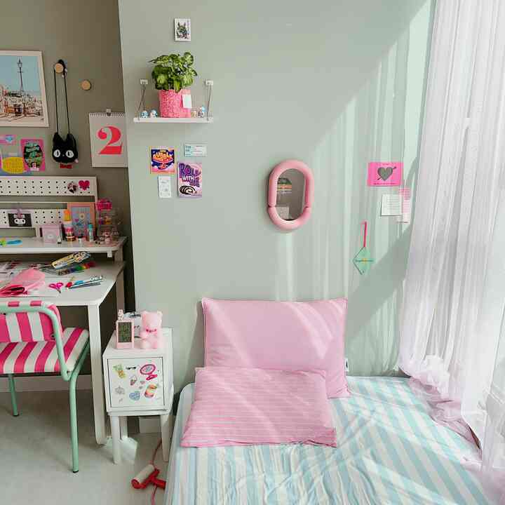 A cozy small single bedroom in pink and mint tones, featuring a desk and bed arranged comfortably