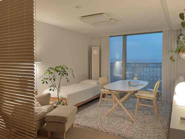 アイボリーと木目調の一人暮らし向けリビング、ダイニングテーブル、アームチェア、ベッドが配置されたナチュラルモダンなインテリア