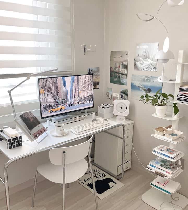White and beige toned home office space featuring a white desk and chair, posters on the wall, and a bookshelf, creating a clean workspace