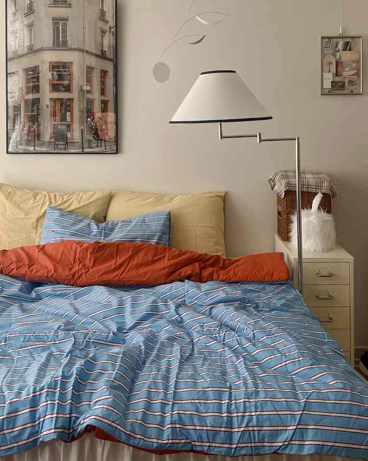 Cozy bedroom with beige walls and pastel-toned bedding, featuring a floor lamp and picture frames in a natural style interior