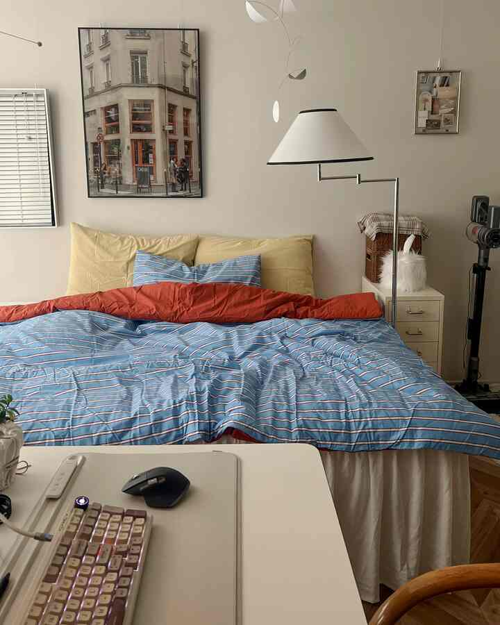 White walls and furniture, blue striped bedding in a studio bedroom with a desk, creating a cozy atmosphere