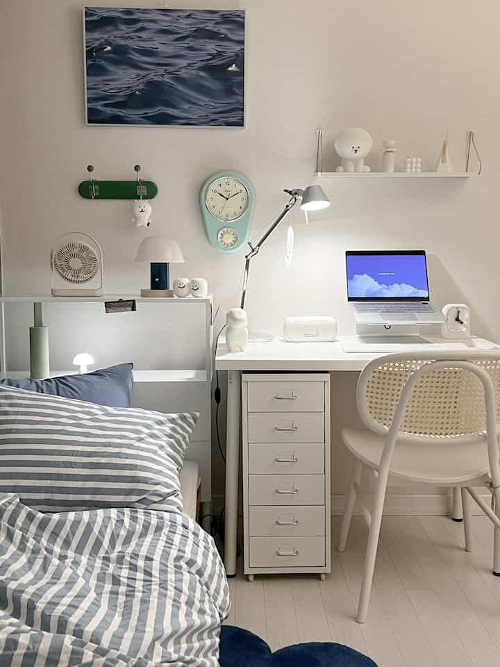 White toned bedroom and home office space featuring blue striped bedding and a neat desk arrangement creating a cozy atmosphere