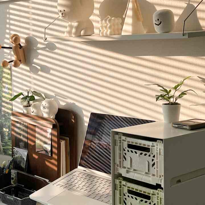 A cozy home office with white and brown tones featuring a laptop, storage drawers, and decorative objets arranged neatly