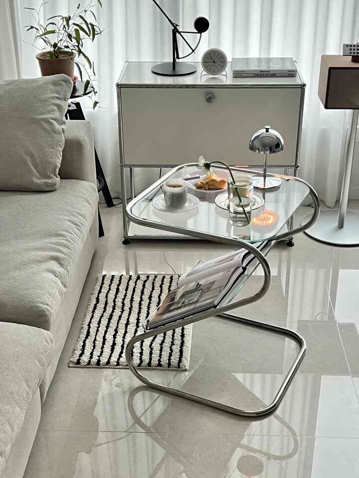 白とグレーの色調のリビング、ベージュのソファとクローム枠のガラスサイドテーブル、ホームカフェ用品が配置されたモダンで雰囲気のあるミッドセンチュリーモダンなインテリア