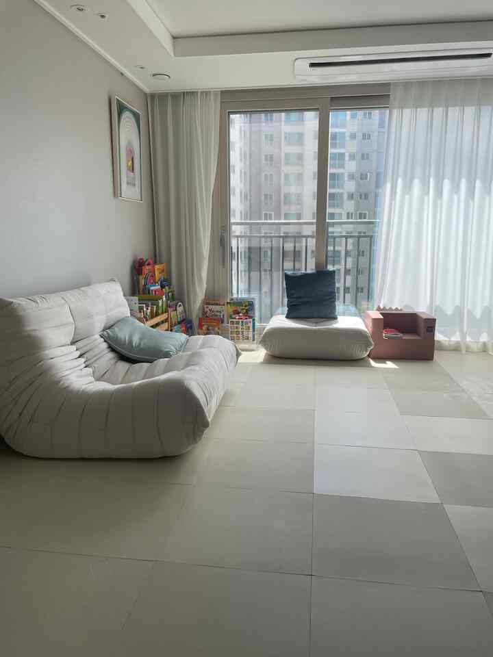 明るいホワイトとベージュの色調のリビング、ソファと子供のおもちゃが配置された小さくて居心地の良い空間